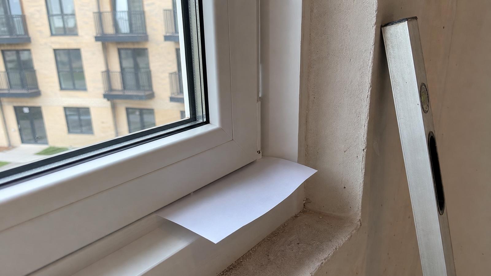 Приёмка окна в новостройке: к притвору оконной створки прижат лист бумаги для проверки на продувание, рядом уровень у откоса